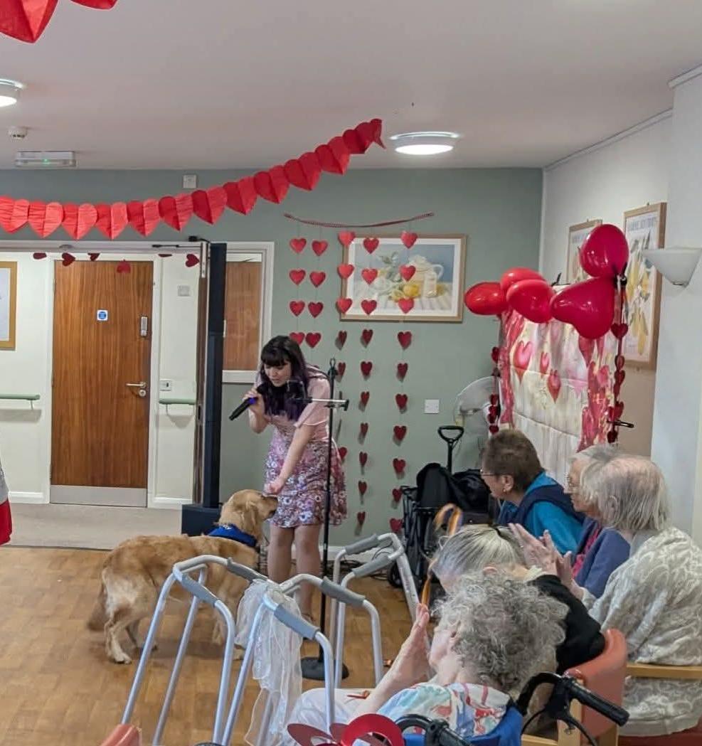 Chelsea singing at a nursing home, and stroking a golden retriever